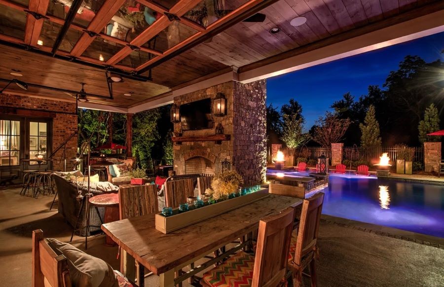 A large outdoor patio area with beautiful lighting, a fireplace, in-ceiling speakers, and a TV.