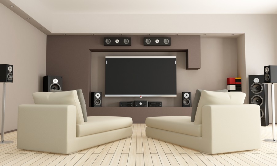 The image is of a living room with surround sound speakers and soundbars installed on the walls and floor.