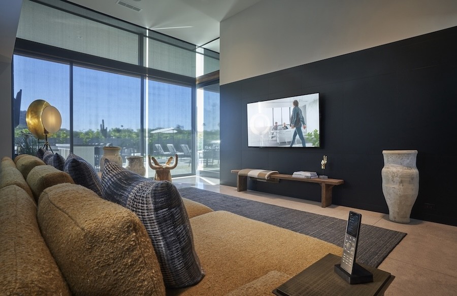 Modern living room with lowered roller shades, wall-mounted TV display, and smart universal remote.