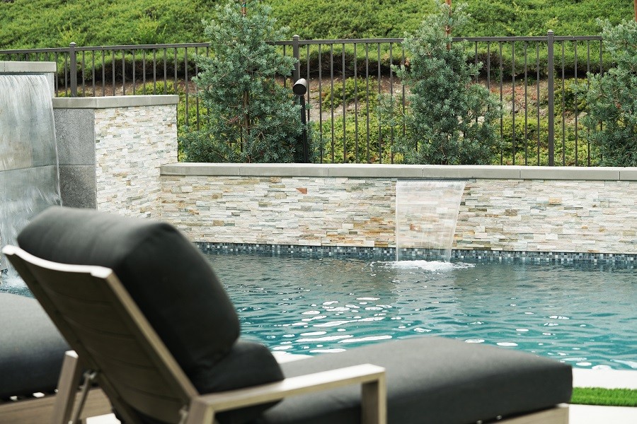 Backyard inground pool with sophisticated tiling, waterfall feature, and landscape speakers playing music.  