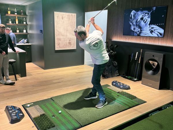 A luxurious indoor golf simulator room with a control panel and immersive screens.