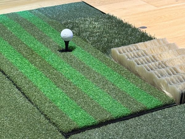 Golfer practicing a swing in an indoor golf simulator bay, standing on a hitting mat facing a large projected virtual golf course.