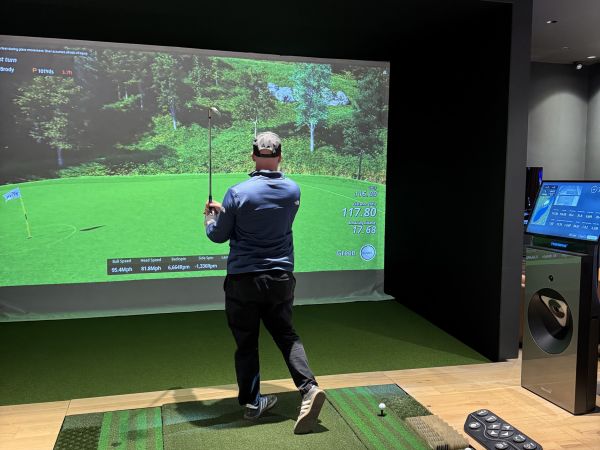 A digital golf simulator view showing a golf course with player metrics and controls.