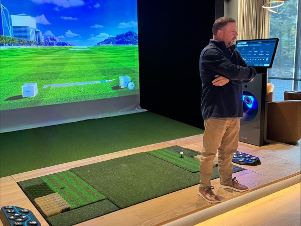 A luxurious indoor golf simulator room with a control panel and immersive screens.